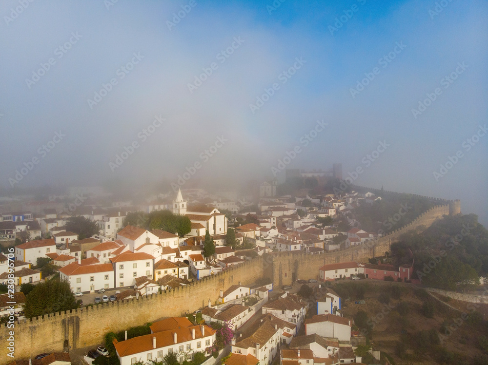 Scenic view of white houses red tiled roofs, and castle from wall of fortress with clouds. Obidos village, Portugal.