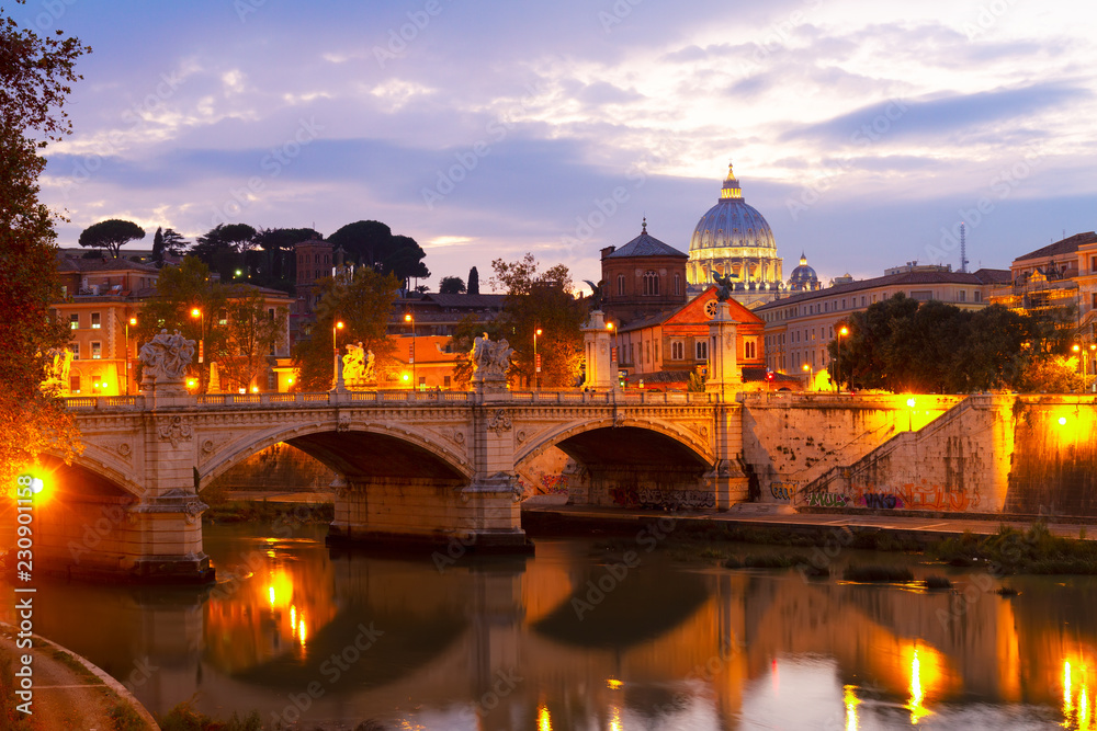 St. Peter's cathedral dome over bridge and river in Rome illuminated at night, Italy