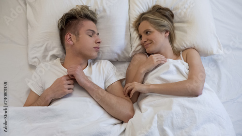 Teenage female waking up and tenderly looking at her sleeping boyfriend, love