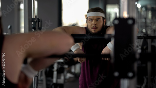 Obraz na plátně Obese male exhausted after workouts in gym, looking at his reflection in mirror