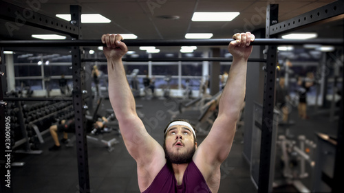 Fotografie Overweight man trying to pull up on sport bar in gym desire to lose extra weight