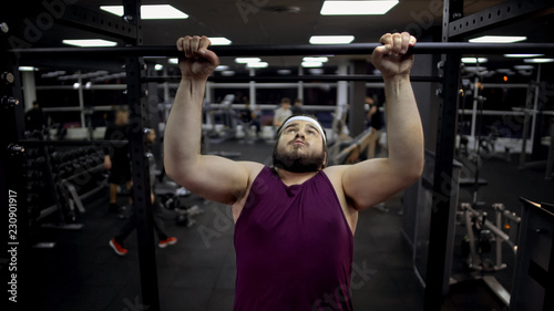 Chubby man pulling up on bar, desire to lose weight and be strong, motivation © motortion