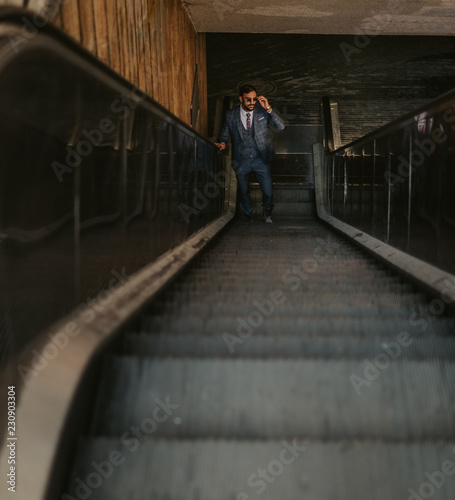 Businessman going up on the escalator while holding sunglasses