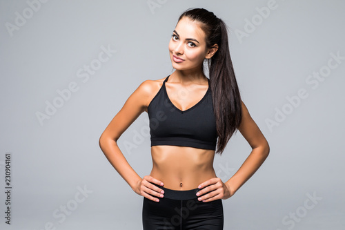 Portrait of sexy young woman with her hands on hips looking at camera. Fitness female with muscular body ready wearing hand gloves for workout on grey background
