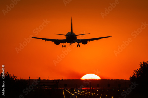 Silhouette of air plane landing on illuminated track at sunset with beautiful red sky and sun in background