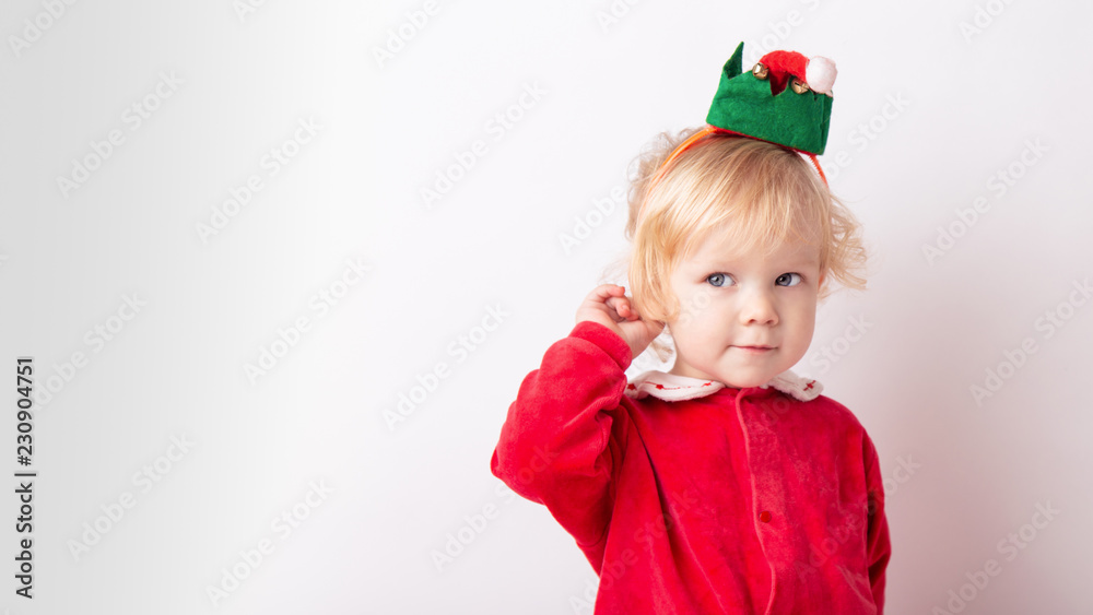 Portrait of cute cute baby girl 1.5 years old, in red clothes And in the cap of the gnome helper Santa.close-up on a white light background. concept christmas Portrait of cute cute baby girl 1.5 years old, in red clothes And in the cap of the gnome helper Santa.close-up on a white light background. concept christmas