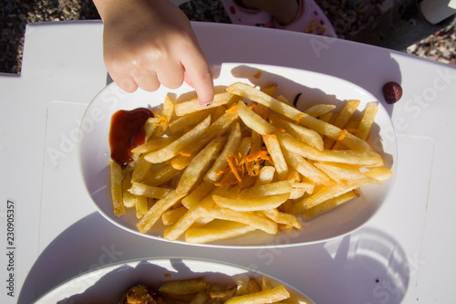 The person carries a plate with mouth-watering French chips. Fried potatoes as a concept of unhealthy fatty foods and fast food. The waiter walks along the beach. Defocussed sea.