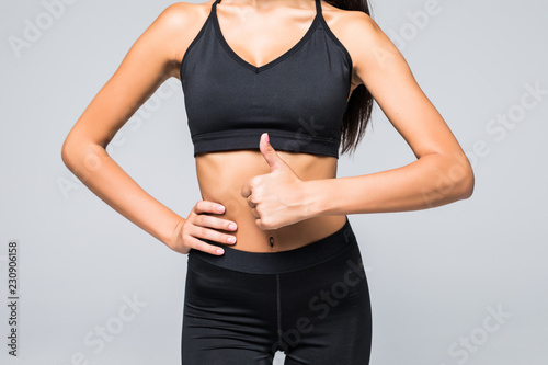 Close up photo of perfect fit slim woman's belly and thumb up on gray background