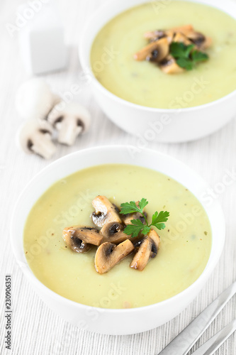 Mushroom cream soup garnished with roasted mushroom slices and parsley, photographed with natural light (Selective Focus, Focus in the middle of the first soup)