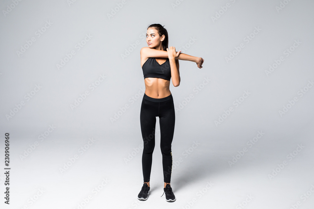 Full length portrait of beautiful young woman doing stretching exercise isolated over gray background Full length portrait of beautiful young woman doing stretching exercise isolated over gray background