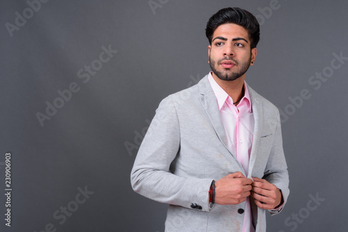 Young handsome Indian businessman against gray background