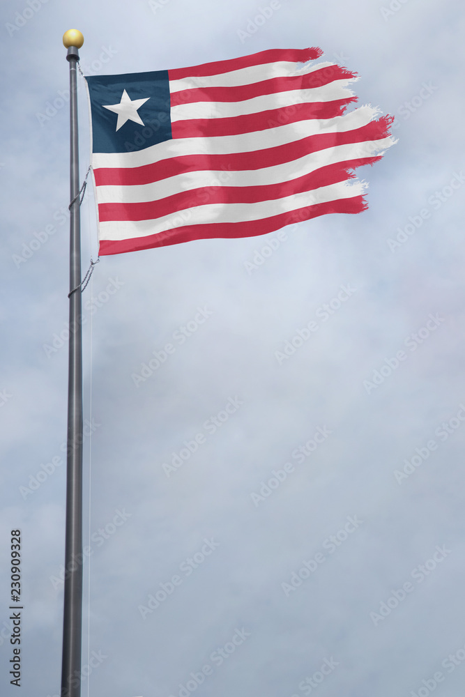 Fototapeta premium Worn and tattered Liberia flag blowing in the wind on a cloudy day