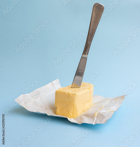 Close up of organic butter unwrapped on paper packaging with knife against blue background (selective focus)