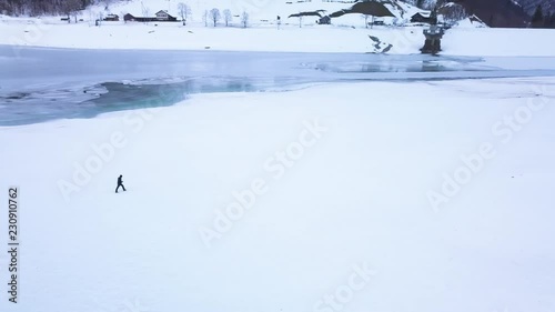 Drone orbits slowly around a man who is walking through a big snow field. In the background is the lake kl√∂ntal which is covered in ice and snow. photo