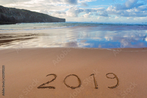 2019 inscription written in the wet yellow beach sand