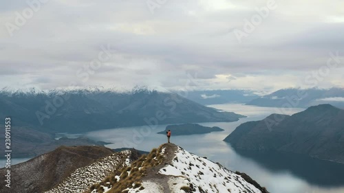 Hiker at the end of a ridge line atop Roys Peak in New Zealand taking photos and looking at view photo