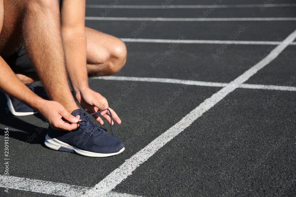 Sporty man tying shoelaces before running at stadium on sunny morning Sporty man tying shoelaces before running at stadium on sunny morning