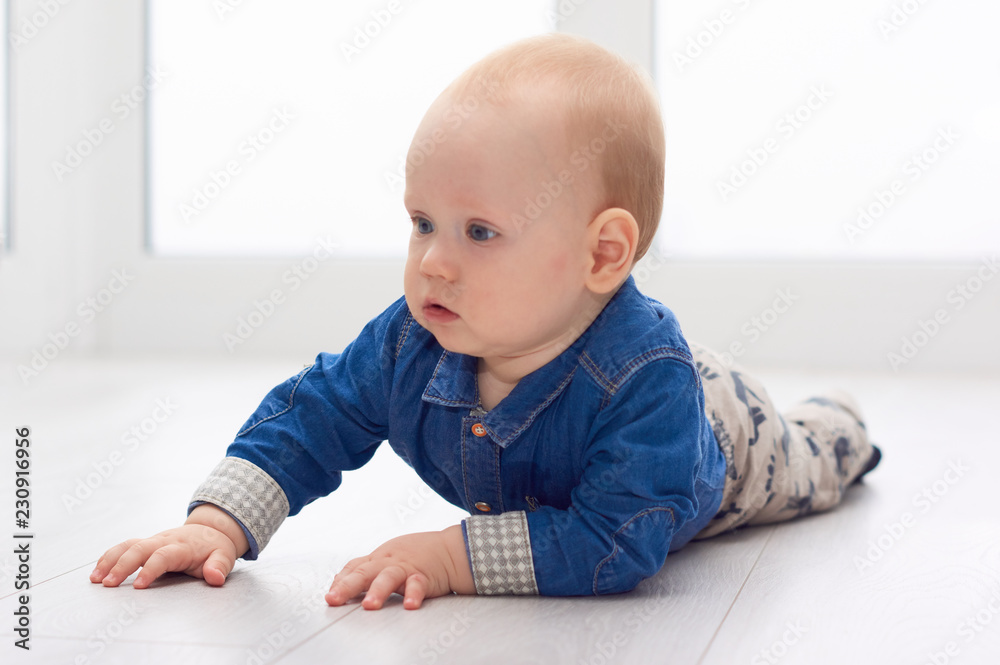 Portrait of a cute little baby in blue denim shirt laying on the floor. Candid image of young baby playing at home/Little baby play on the floor Portrait of a cute little baby in blue denim shirt laying on the floor. Candid image of young baby playing at home/Little baby play on the floor