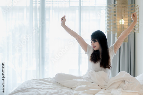 Asian Woman stretching in bed after wake up in bedroom at home.