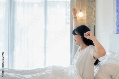 Asian Woman stretching in bed after wake up in bedroom at home.