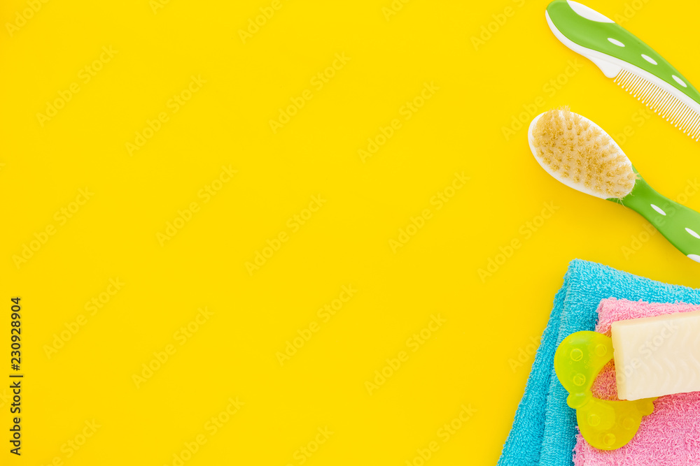 Baby care. Bath cosmetics and accessories for child. Shampoo, gel, cream, comb, yellow rubber duck on yellow background top view space for text