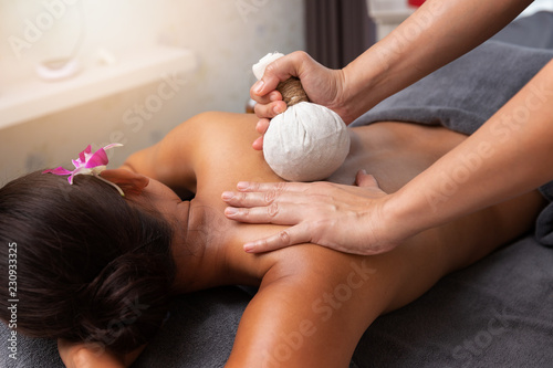 Asian woman enjoying compress balls, herbal ball massage at spa.
