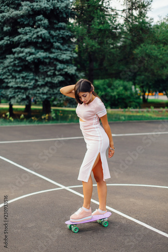 Portrait of a smiling charming brunette female standing on her skateboard on a basketball court.