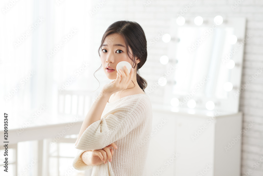 Attractive young Korean woman applying face powder in her make-up room Attractive young Korean woman applying face powder in her make-up room