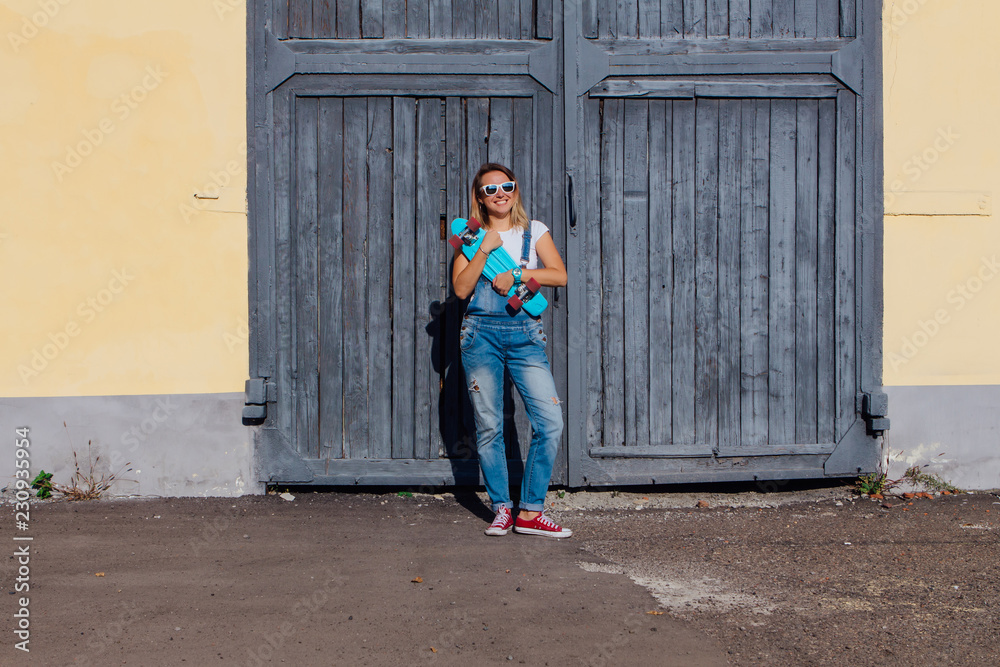 Portrait of a smiling woman standing with her skateboard next to the old wooden wall. Portrait of a smiling woman standing with her skateboard next to the old wooden wall.