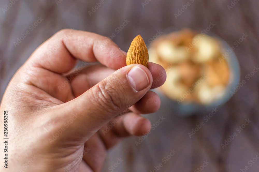 A person showing and offering an almond from a bowl A person showing and offering an almond from a bowl