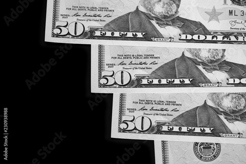 A pack of fifty dollar bills on a dark background. Black and white