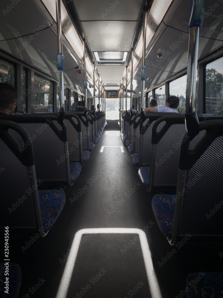 Inside the top deck of a bus during the day, with passengers. Looking down the aisle