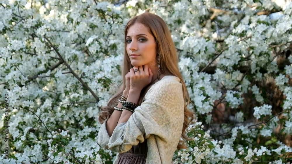 Beautiful young woman in long dress boho style under apple tree in blossom in garden Beautiful young woman in long dress boho style under apple tree in blossom in garden