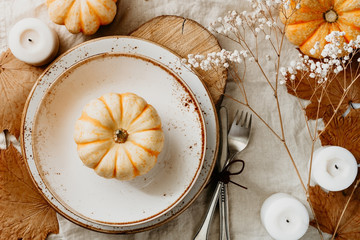 Top view on a decorated table setting for Thanksgiving dinner. Autumn ornate, white pumpkin on ceramic plates.