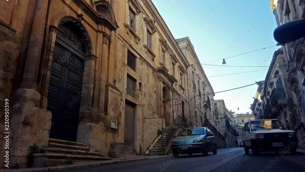 Historical street of Modica, Sicily - Italy. Old buildings with stairs. Cars comes toward the camera. Historical street of Modica, Sicily - Italy. Old buildings with stairs. Cars comes toward the camera.