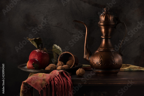 Still life with a copper jug, apples and nuts on a wooden table photo