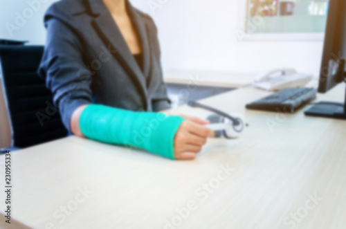 blurred woman with broken hand and green cast  working on computer in office