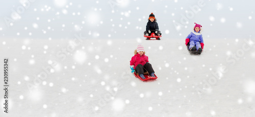 childhood, sledging and season concept - group of happy little kids sliding on sleds down snow hill in winter
