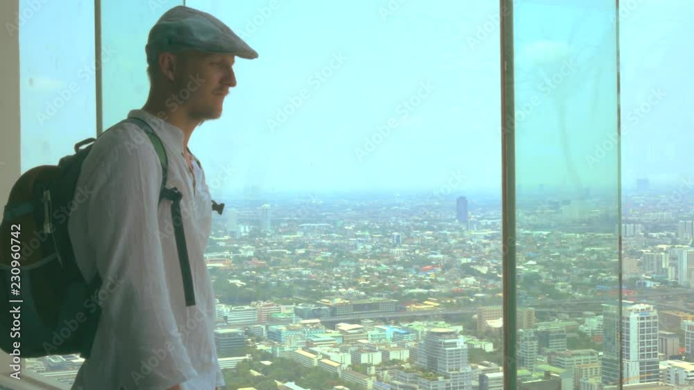 A man traveler in a cap looks at the city through a skyscraper window A man traveler in a cap looks at the city through a skyscraper window
