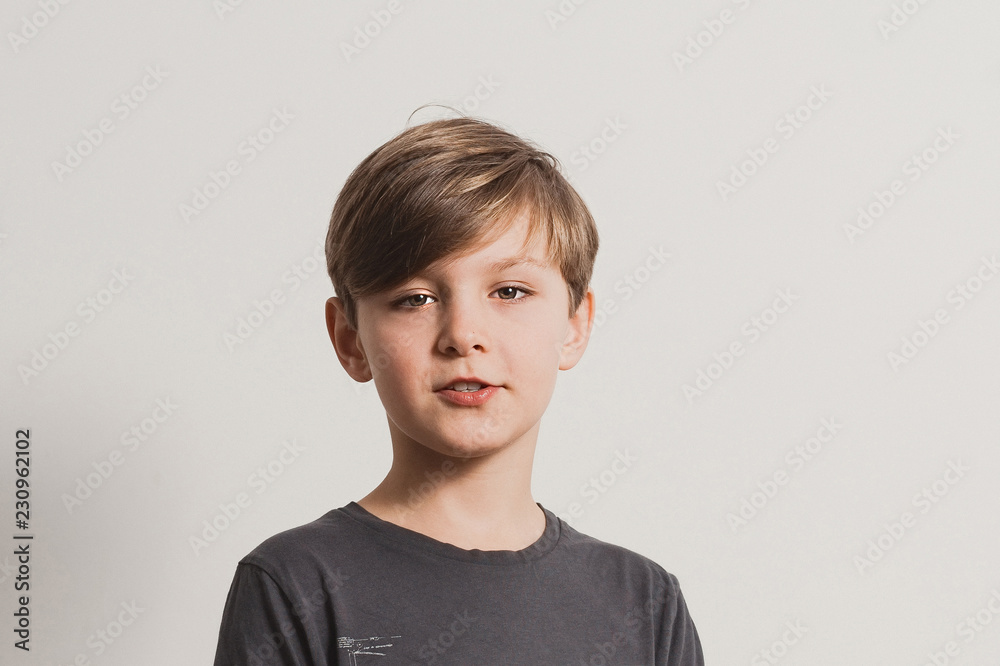 a portrait of cute boy saying something, looking at camera, dark grey shirt, white wall. Copy space for your text and design a portrait of cute boy saying something, looking at camera, dark grey shirt, white wall. Copy space for your text and design