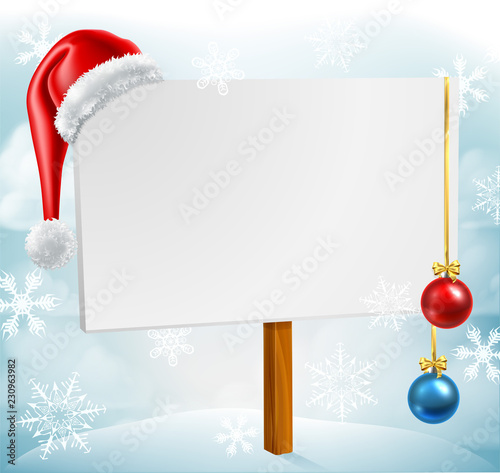 A Christmas sign with a Santa Claus hat and bauble decorations in a winter snow scene with snowflakes falling