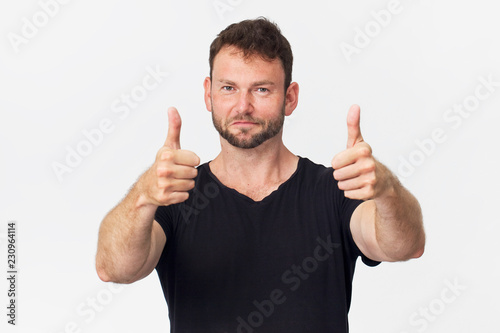 Smiling young man giving thumbs ups wearing black t-shirt isolated on white photo