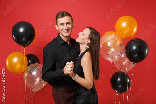 Stunning young couple in black clothes celebrating birthday holiday party isolated on bright red background air balloons. St. Valentine's International Women's Day Happy New Year 2019 concept. Mock up