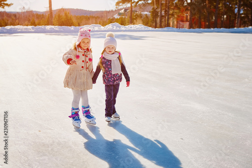 Two little girls hold hands and skate. Space for text