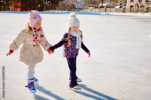 Two little girls hold hands and skate.