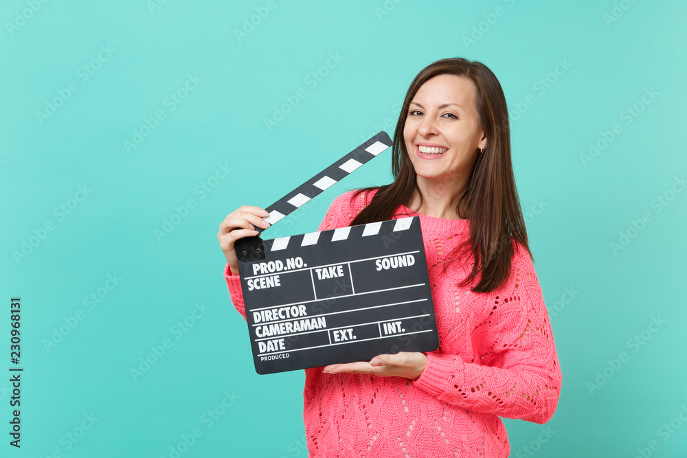 Stunning young woman in knitted pink sweater hold in hand classic black film making clapperboard isolated on blue turquoise background, studio portrait. People lifestyle concept. Mock up copy space.