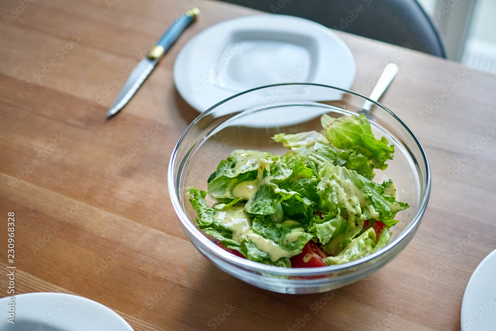Fresh Vegetable Dish. Vegetables in a transparent bowl on a wooden dinner table. Ingredients: slices of red tomato and green salad leaves sprinkled with olive (or sunflower) oil and sauce Fresh Vegetable Dish. Vegetables in a transparent bowl on a wooden dinner table. Ingredients: slices of red tomato and green salad leaves sprinkled with olive (or sunflower) oil and sauce