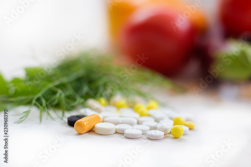 The heap of tablets, drugs lies against the background of fresh vegetables