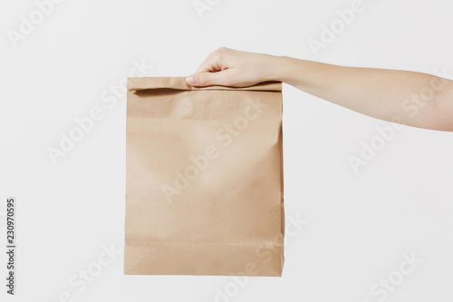 Close up female holds in hand brown clear empty blank craft paper bag for takeaway isolated on white background. Packaging template mockup. Delivery service concept. Copy space. Advertising area.