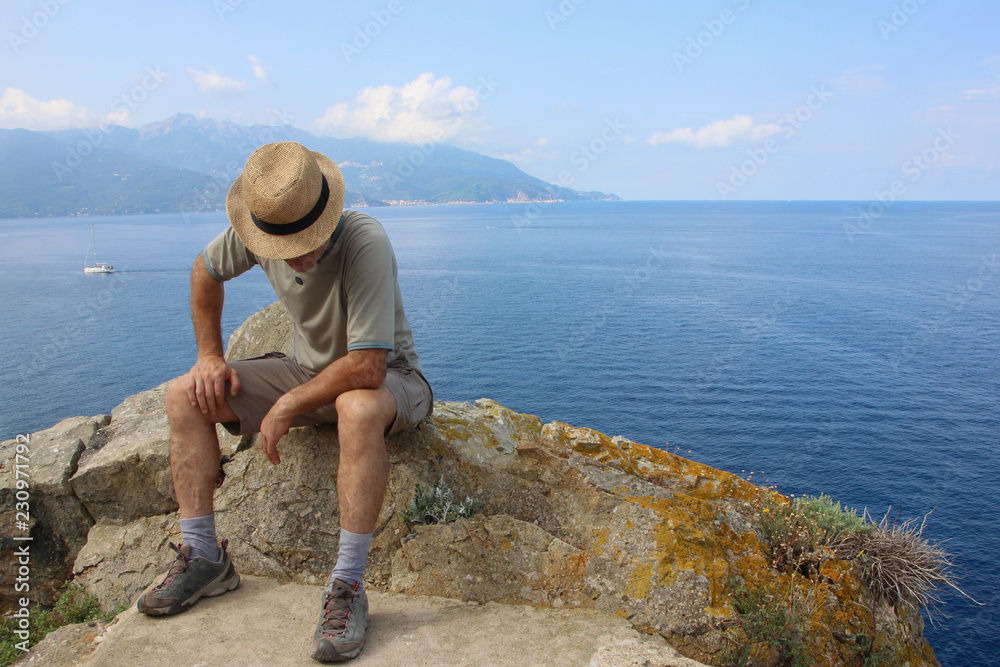 Man with a straw hat resting on a rock in Elba island, Enfola headland, Italy